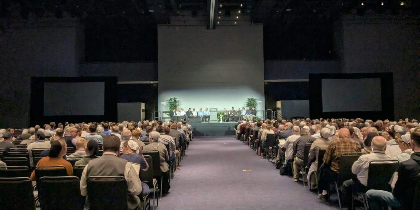 Attendees seated in a conference hall facing the REACH stage
